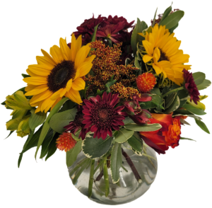 Flower arrangement in Fall colors featuring sunflowers, chrysanthemums, roses, and other flowers in a clear glass ginger jar style vase.