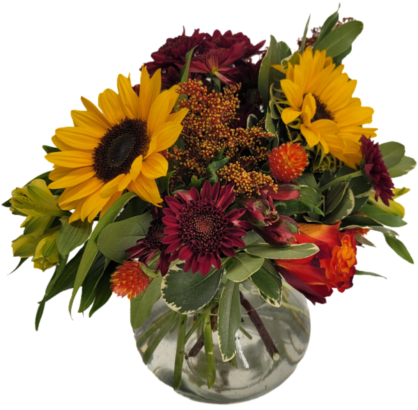 Flower arrangement in Fall colors featuring sunflowers, chrysanthemums, roses, and other flowers in a clear glass ginger jar style vase.